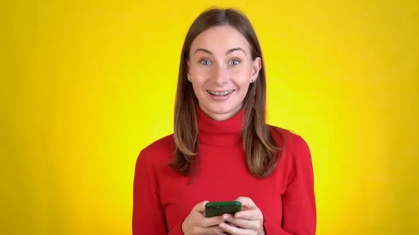 Αστεία νεαρή γυναίκα που ποζάρει απομονωμένη στο κίτρινο στούντιο. Η έννοια του τρόπου ζωής. Χρησιμοποιώντας κινητό τηλέφωνο πληκτρολογώντας sms περιήγηση μήνυμα πω wow καλύπτει το στόμα με ανοιχτό — Φωτογραφία Αρχείου