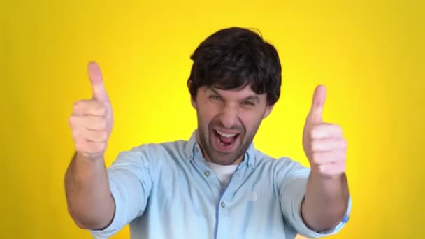 Guapo chico sonriente aislado sobre fondo amarillo en el estudio. Gente emociones sinceras, concepto de estilo de vida. Mira con aprobación apuntando con los dedos a la cámara mostrando los pulgares hacia arriba — Vídeo de stock