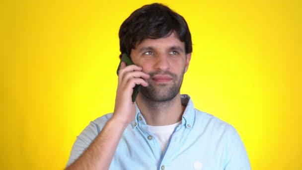 Hombre sonriente que habla por teléfono móvil llevando a cabo una agradable conversación aislada sobre fondo amarillo en el estudio. Concepto de vida — Vídeo de stock