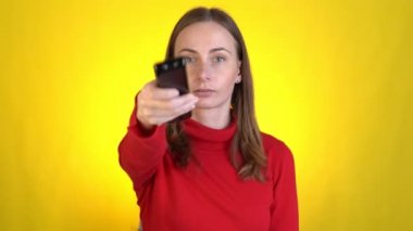 Kadın uzaktan kumandayla kanal değiştiriyor sarı arka planda televizyon izliyor. Adam en sevdiği programı izliyor