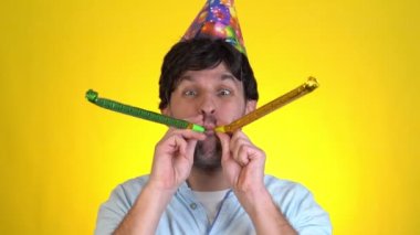 Doğum günü şapkalı genç adam sarı arka planda kutlama yapıyor..