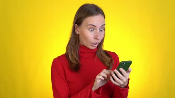노란 배경 스튜디오에 고립 된 젊은 여자가 웃는 거야. 사람들의 생활 방식. 휴대폰 입력 sms 문자를 사용하여 오픈으로 입을 덮는 와우라고 말 할 수있습니다 — 비디오