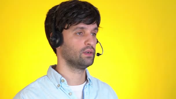 Homem de sucesso no fone de ouvido gesticulando e falando na câmera em um fundo amarelo. Conceito de tecnologia e comunicação online. — Vídeo de Stock