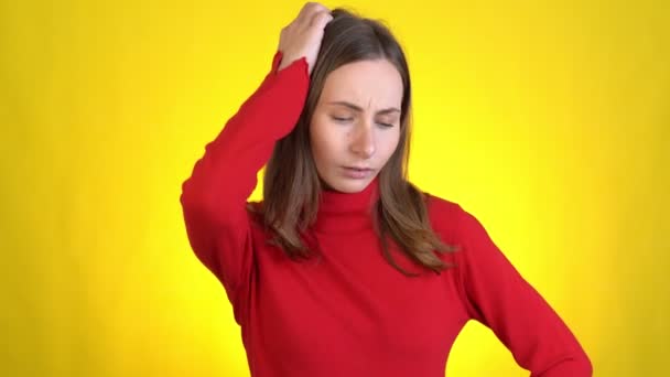 Jeune femme isolée sur fond jaune en studio. Les gens émotions sincères, concept de style de vie. Regarde la caméra, pense, rayures au temple vient avec des idées — Video