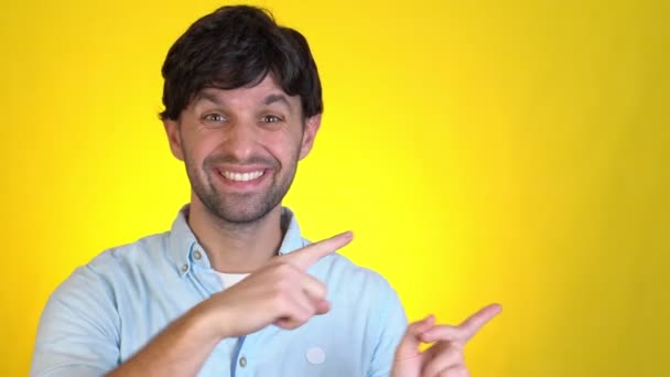 Smiling excited man posing isolated on yellow background studio. People lifestyle concept. Pointing index fingers hands aside camera doing winner gesture — Stock Video