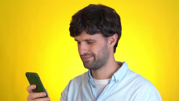 Overrasket mand isoleret på gul baggrund studie. Brug mobiltelefon hold fan af kontanter penge i dollar sedler – Stock-video