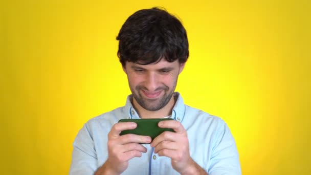 Szerencsejáték fiatal férfi játszani mobiltelefon hold szerkentyű okostelefon videó pc játékok elszigetelt sárga háttér stúdió Emberek életmód koncepció — Stock videók