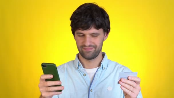 Happy man használata hold in hand credit bank kártya mobiltelefon most derült ki, nagy győzelem hír elszigetelt sárga háttér stúdió emberek életmód koncepció — Stock videók