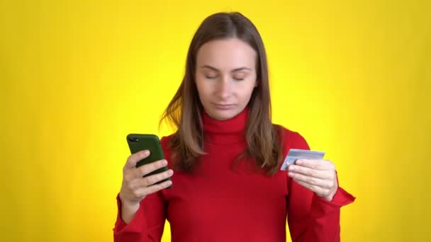 Happy woman using hold in hand credit bank card mobile phone just found out great big win news isolated on yellow background studio Emberek életmód koncepció. — Stock videók