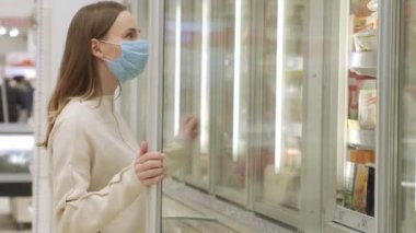 Tıbbi maskeli bir kadın süpermarketten donmuş yiyecek alıyor..