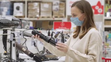 Antivirüs maskesi takan beyaz bir kadın alet dükkanından saç kurutma makinesi seçiyor. Salgın sırasında alışveriş kavramı