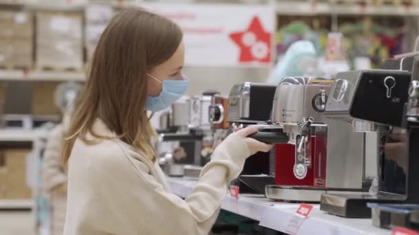 Feminino em um cliente máscara médica escolhendo máquina de café na loja de eletrônicos — Vídeo de Stock