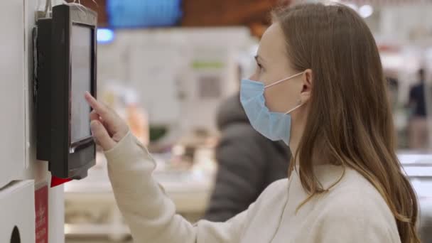 Жінка в медичній масці використовує електронну інформаційну дошку в громадському місці . — стокове відео