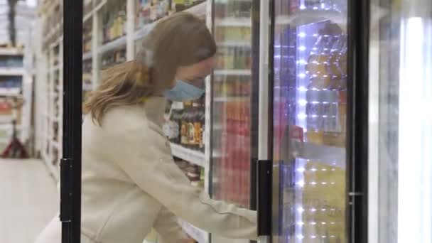 Mulher em uma máscara médica selecionando uma cerveja no supermercado — Vídeo de Stock