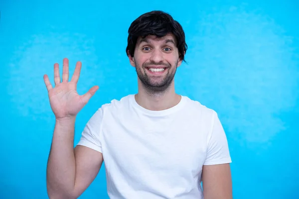 Joven hombre guapo de pie sobre fondo azul mostrando y señalando hacia arriba con los dedos número cinco mientras sonríe confiado y feliz. —  Fotos de Stock