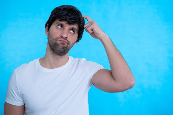 El hombre tiene dudas mientras rasca la cabeza sobre un fondo azul aislado —  Fotos de Stock