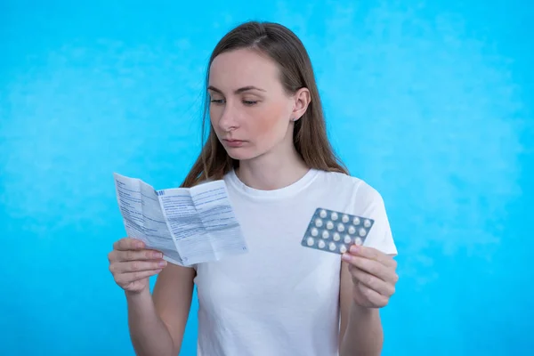 Mujer joven con drogas y pastillas. Mujer enferma mirando la explicación del medicamento antes de tomar medicamentos recetados en un fondo azul — Foto de Stock