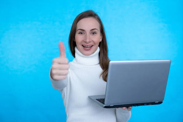 Retrato de una joven excitada sosteniendo computadora portátil y celebrando el éxito aislado sobre fondo azul —  Fotos de Stock