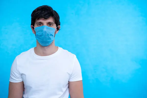 青い背景に医療マスクをした肖像画の男。健康を守るんだ。コロナウイルスの概念 — ストック写真