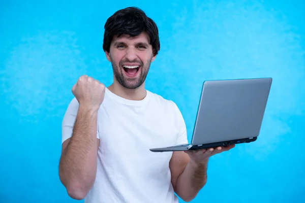 Portrait of an excited man holding laptop computer and celebrating success isolated over blue background Royalty Free Stock Images