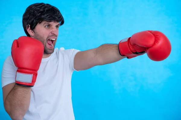 Immagine di un giovane pugile urlante che posa isolato su una parete di sfondo blu indossando guanti da boxe. — Foto Stock