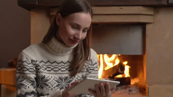 Vrouw met een digitale tablet zit bij de open haard — Stockfoto