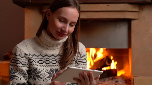 Vrouw met een digitale tablet zit bij de open haard — Stockfoto