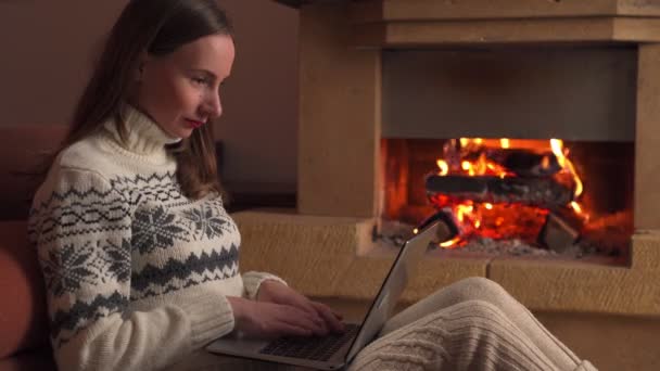 Молодая женщина празднует успех или счастливую позу с ноутбуком перед камином — стоковое видео