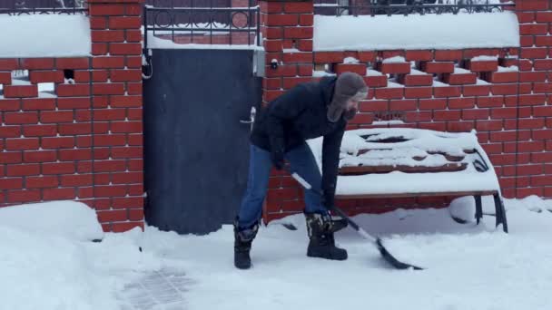 Młody człowiek usuwa śnieg w pobliżu domu na przedmieściach. — Wideo stockowe