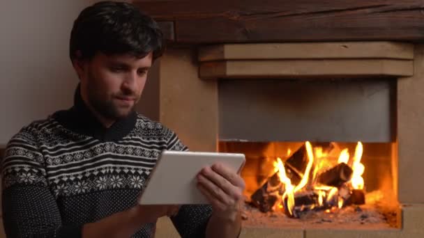 Hombre usando una tableta digital se sienta junto a la chimenea — Vídeo de stock