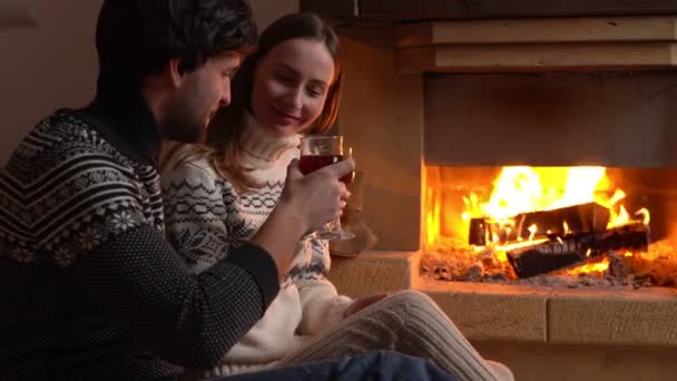 Молодая романтическая пара сидит перед камином дома, пьет красное вино. — стоковое видео