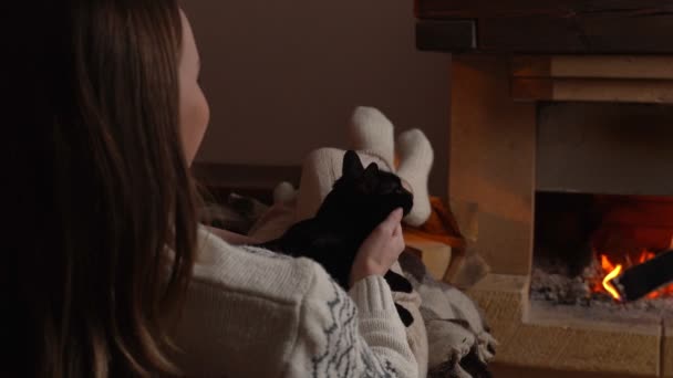 Жінка руки улюбленця милий чорний кіт спить на колінах перед каміном — стокове відео