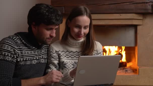 Lachend paar zit op de vloer en met behulp van een laptop en surfen op het internet thuis — Stockvideo