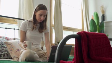 Dizüstü bilgisayarda çalışan güzel bir kadın evdeki yatakta oturuyor..