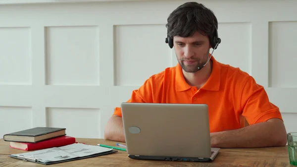 Man uses a headset to talk online at his workplace, confident man sits at the office desk and looks at laptop screen — Stock Photo, Image