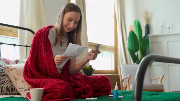 La mujer lee las instrucciones de la píldora, sentada en la cama cubierta con una manta — Foto de Stock