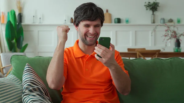 Удивлен счастливый мужчина держит телефон глядя на сотовый телефон читать хорошие новости в смс на диване — стоковое фото