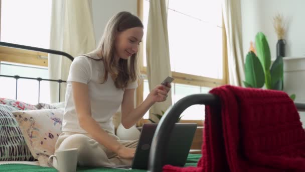 Woman holding a credit card in her hand is trying to buy something online while lying on the couch — Stock Video