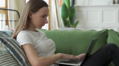 Evdeki koltukta dizüstü bilgisayar kullanan kadın.