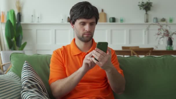 Überraschter glücklicher Mann mit Handy liest gute Nachrichten in SMS auf dem Sofa — Stockvideo