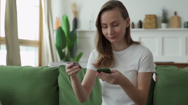 Giovane donna che acquista online con carta di credito e smartphone mentre è seduta sul divano di casa. — Video Stock