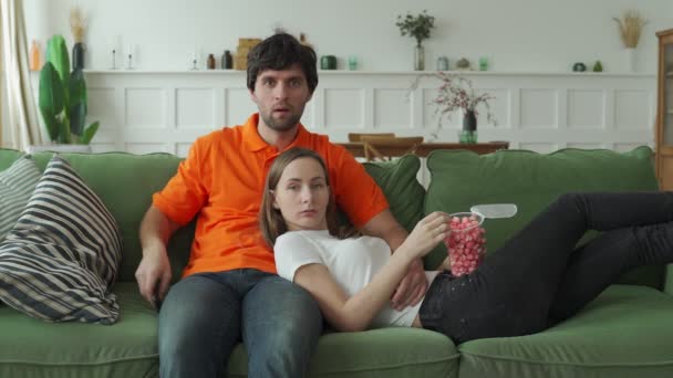 Junges Paar schaut Fernsehen mit Popcorn auf Couch — Stockvideo