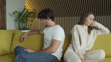 İlişki sorunları yaşayan genç çift sarı bir kanepede yan yana oturuyor.