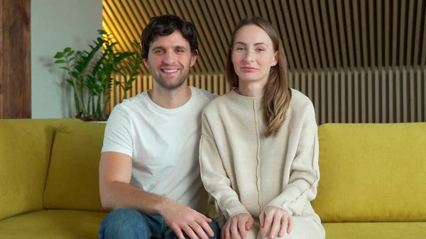 Портрет жены и мужа, размахивающих руками, смотрящих в камеру и говорящих "привет", сидящих на диване в гостиной — стоковое фото