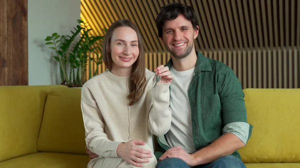 Молодая пара с ключом от нового дома сидит на жёлтом диване — стоковое фото