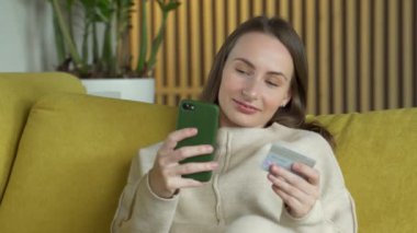 İnternetten kredi kartı ve akıllı telefonuyla satın alan bir kadın evdeki sarı koltukta oturuyor.