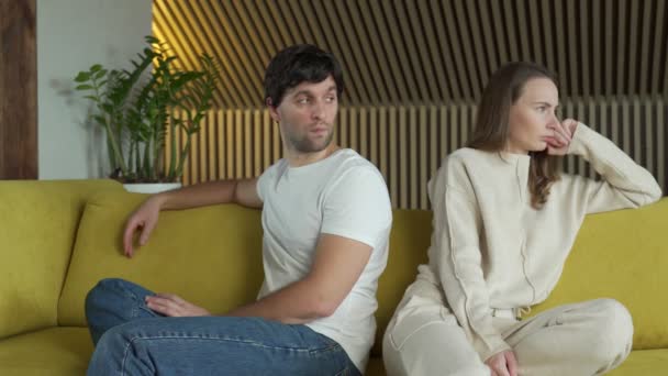Молодая пара испытывает проблемы в отношениях сидит рядом друг с другом дома на желтом диване — стоковое видео