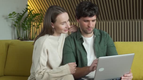 Portrét usmívajícího se mladého páru pomocí notebooku, zatímco sedí doma na žluté pohovce — Stock video