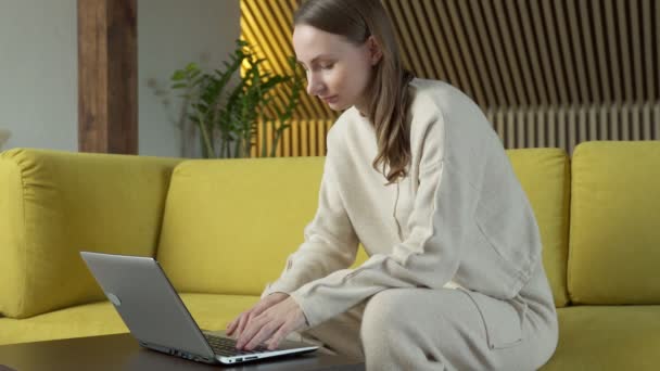 Kobieta pracująca na laptopie, siedząca na żółtej sofie w domu — Wideo stockowe