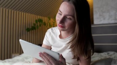 Kadın gece geç saatlerde yatakta yatarken dijital tablette blog okuyor.